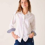 Woman wearing a white shirt with patterned cuffs against a plain background