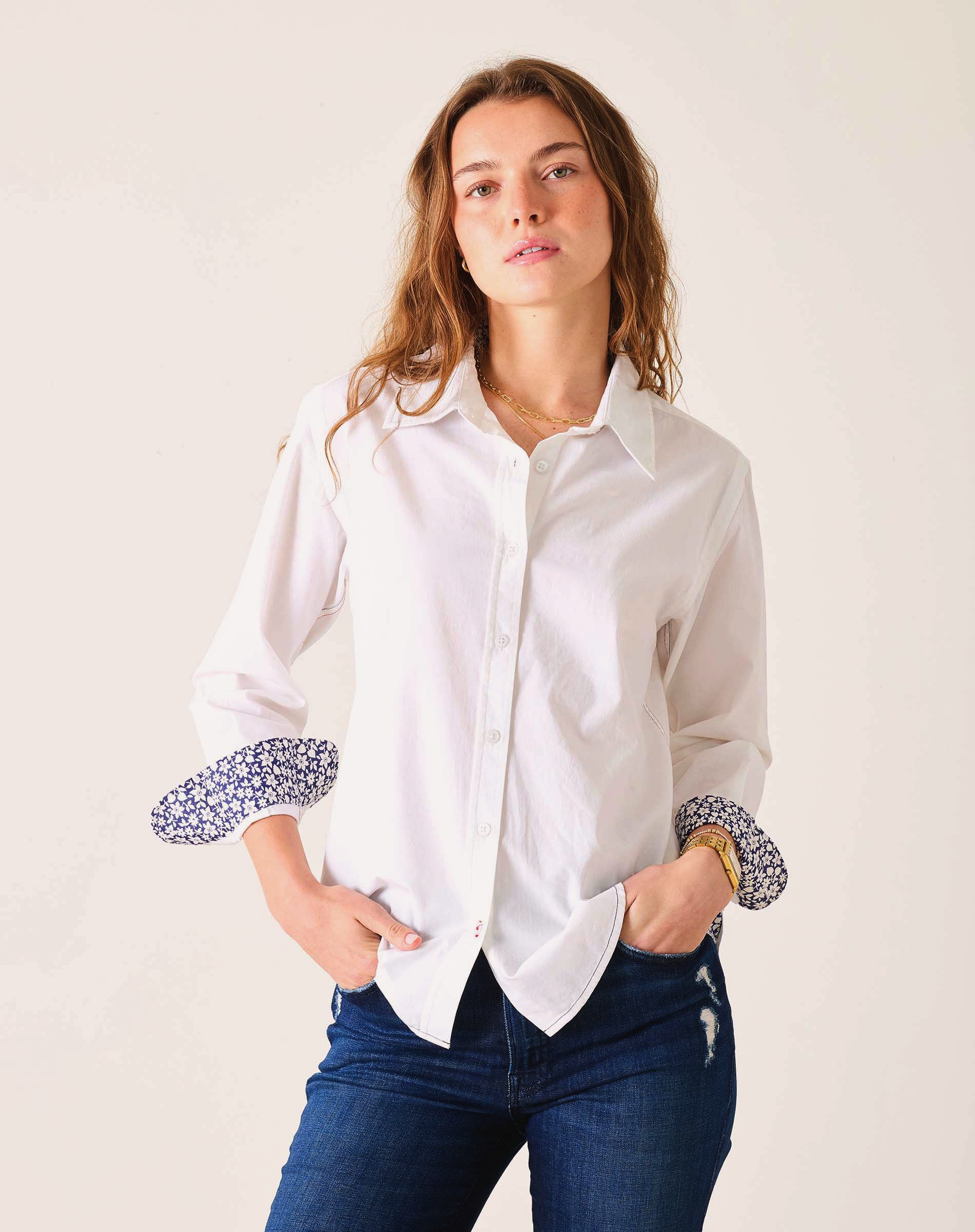 Woman wearing a white shirt with patterned cuffs against a plain background