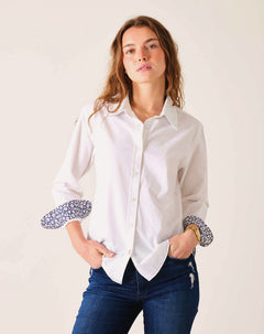 Woman wearing a white shirt with patterned cuffs against a plain background