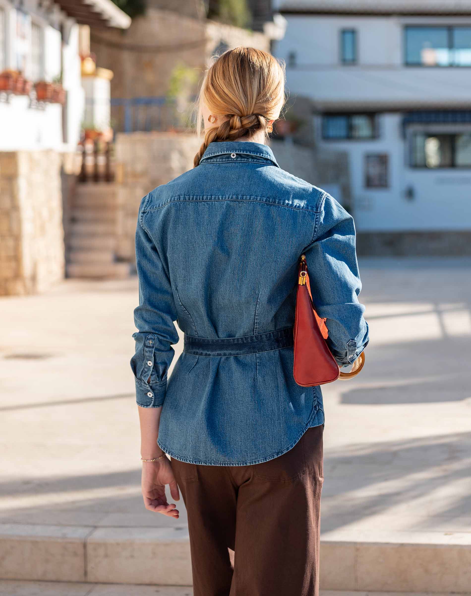 Back view of a blue chambray button-up shirt with a waist tie and long sleeves.