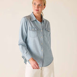 Woman wearing a light blue denim shirt against a plain background