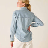 Woman wearing a light blue denim shirt against a beige background