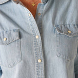 Light blue denim shirt with gold buttons and a necklace featuring a butterfly pendant.