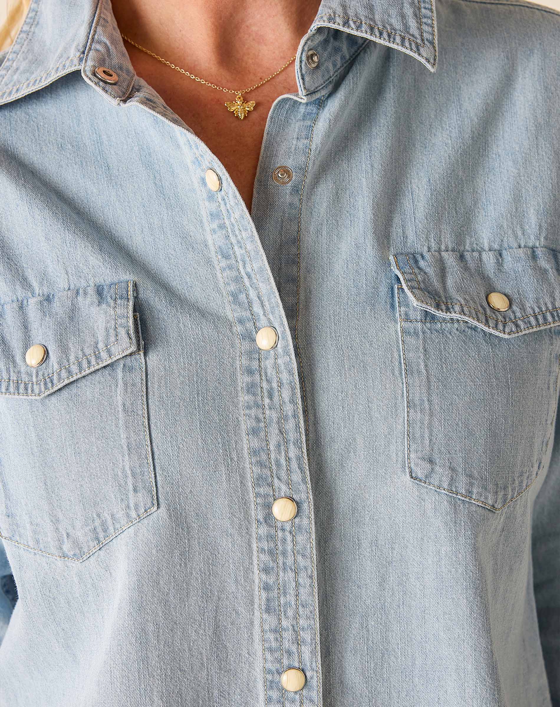 Light blue denim shirt with gold buttons and a necklace featuring a butterfly pendant.