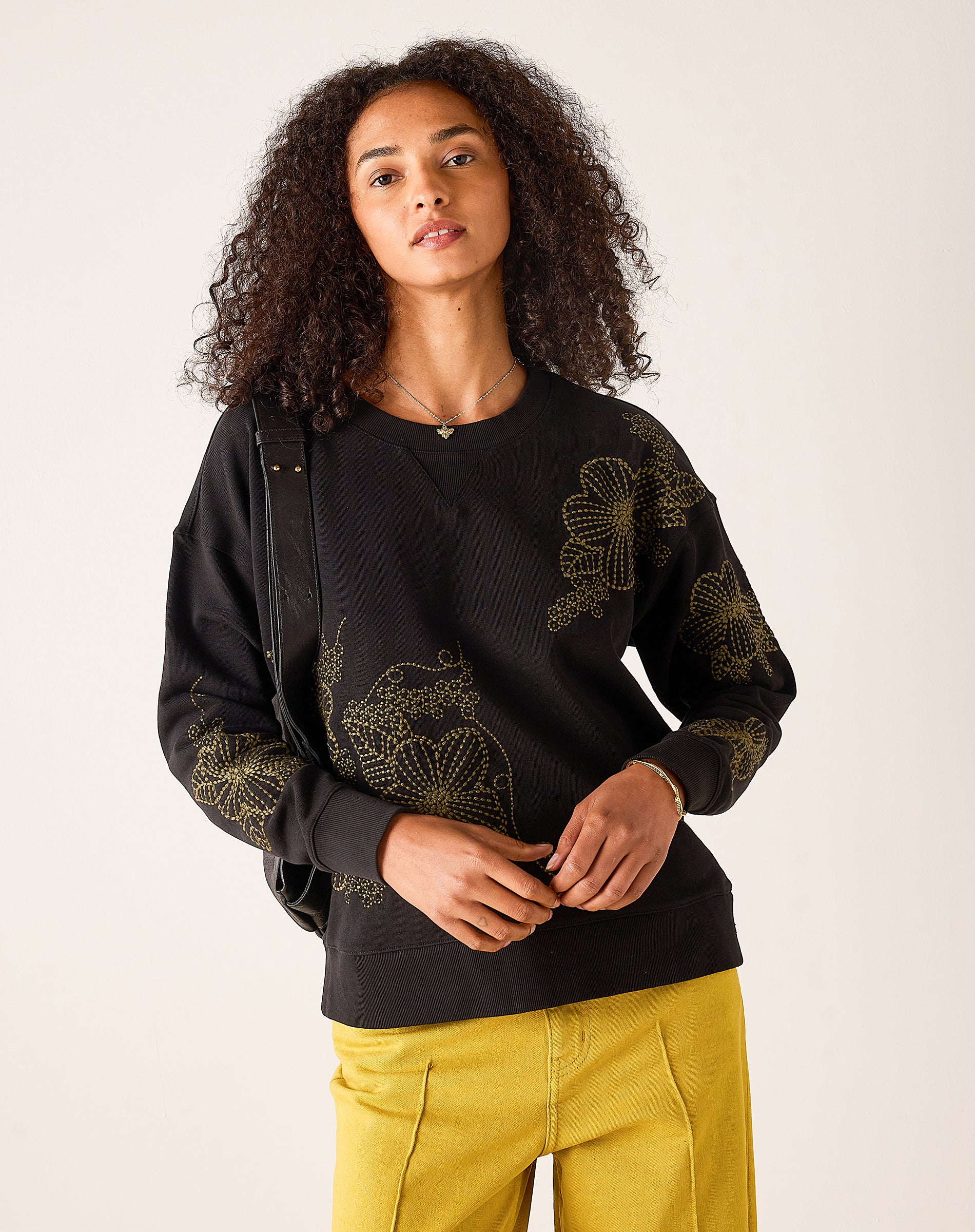 Women's travel-friendly black knit sweatshirt with gold-toned floral embroidery and a V-neckline.