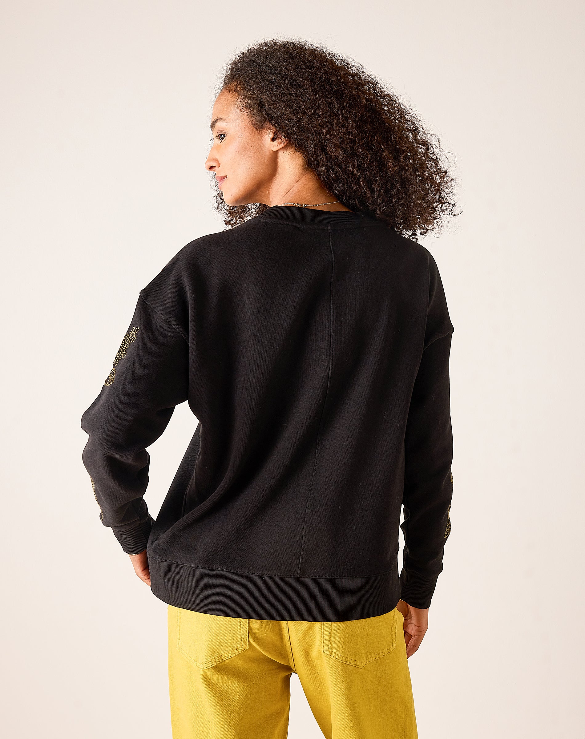 Back view of a black sweatshirt featuring an embroidered detail on the sleeve.
