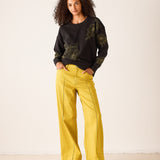 Dark charcoal crewneck sweatshirt with large yellow and white floral embroidery, paired with mustard yellow wide-leg trousers.