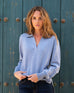 female wearing blue collared v neck polo sweater in front of a blue wooded wall