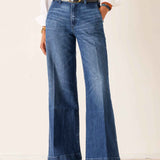 Person wearing blue flared jeans with a white shirt on a plain background