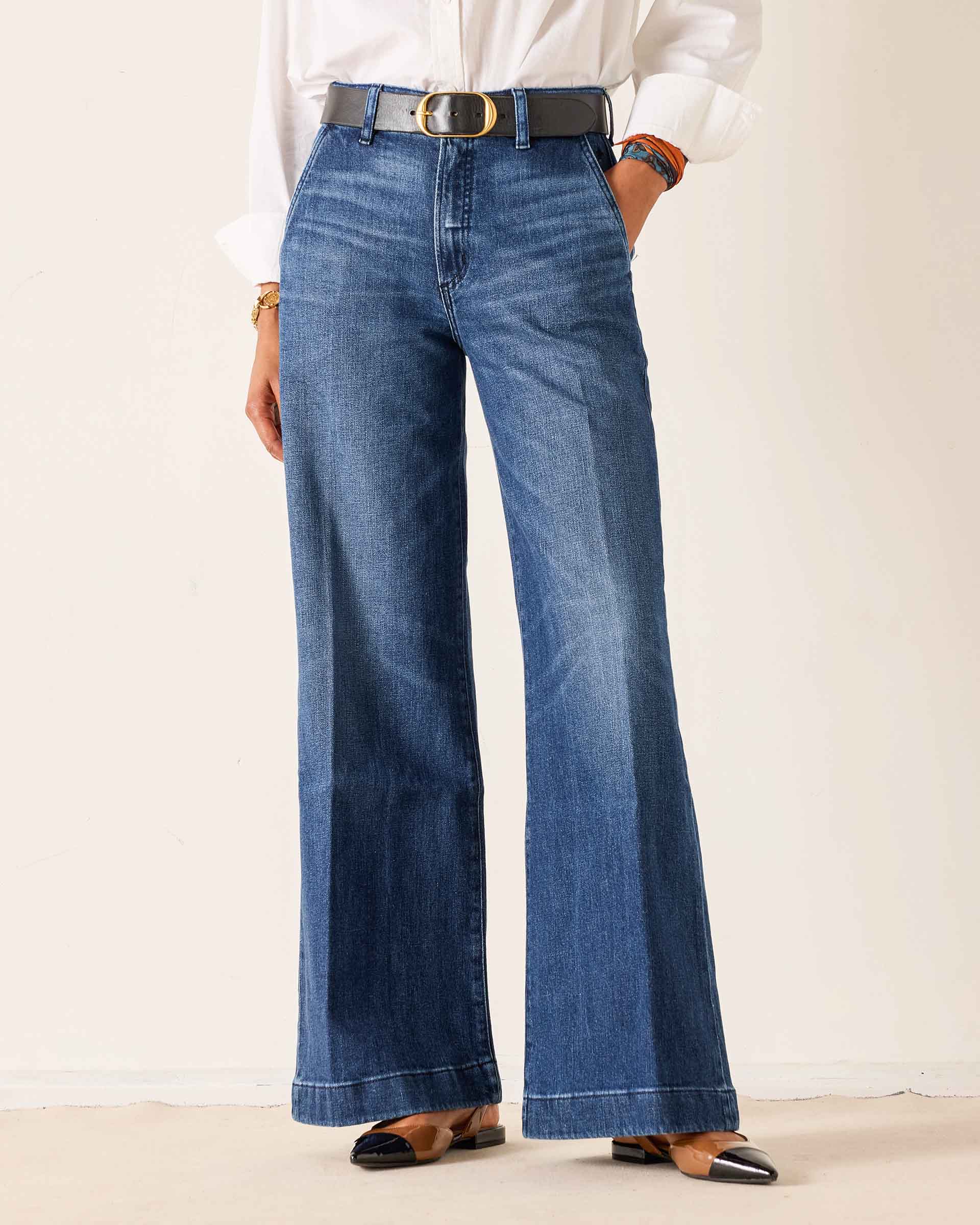 Person wearing blue flared jeans with a white shirt on a plain background
