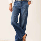 Person wearing blue jeans with a white shirt and black shoes on a plain background