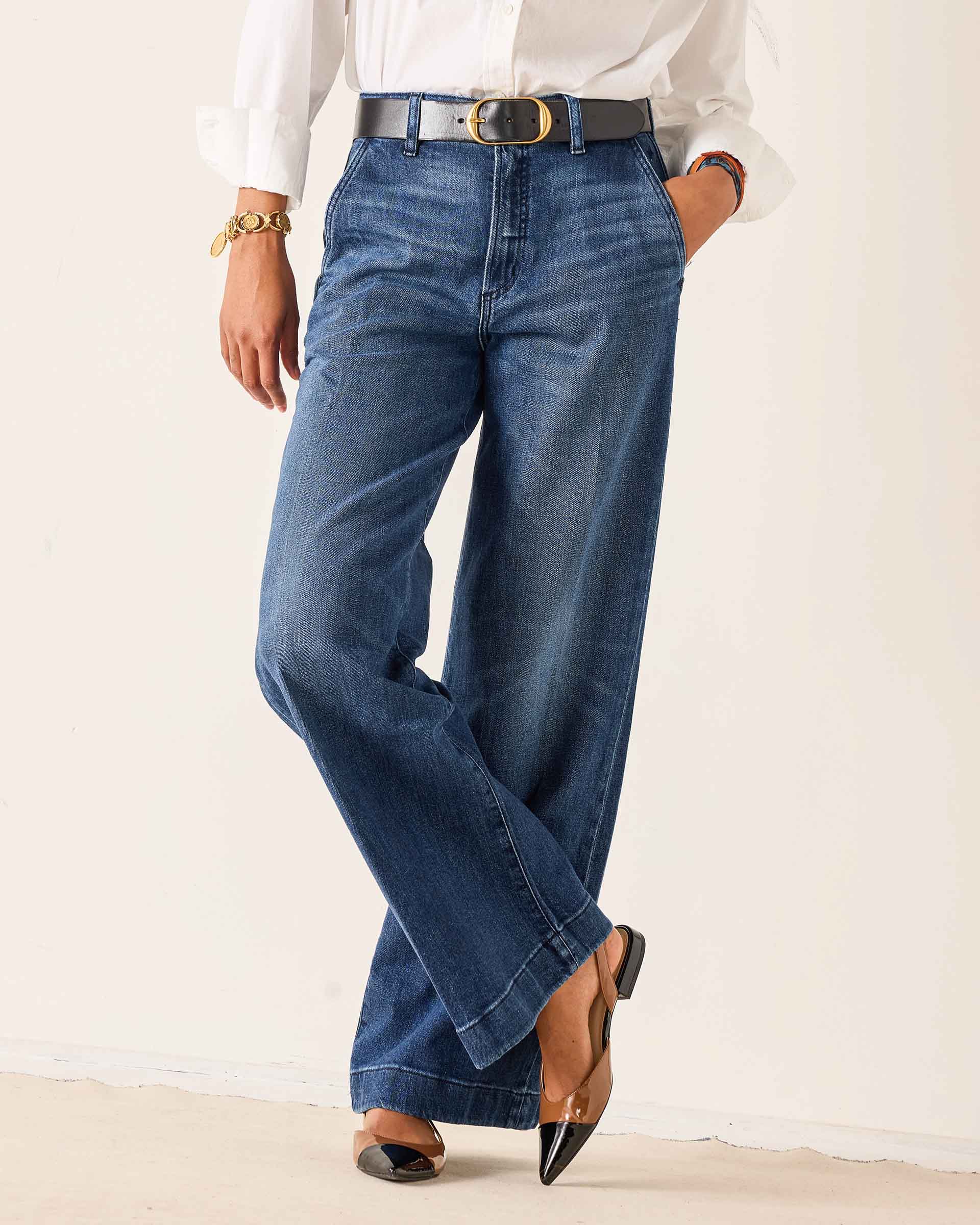 Person wearing blue jeans with a white shirt and black shoes on a plain background
