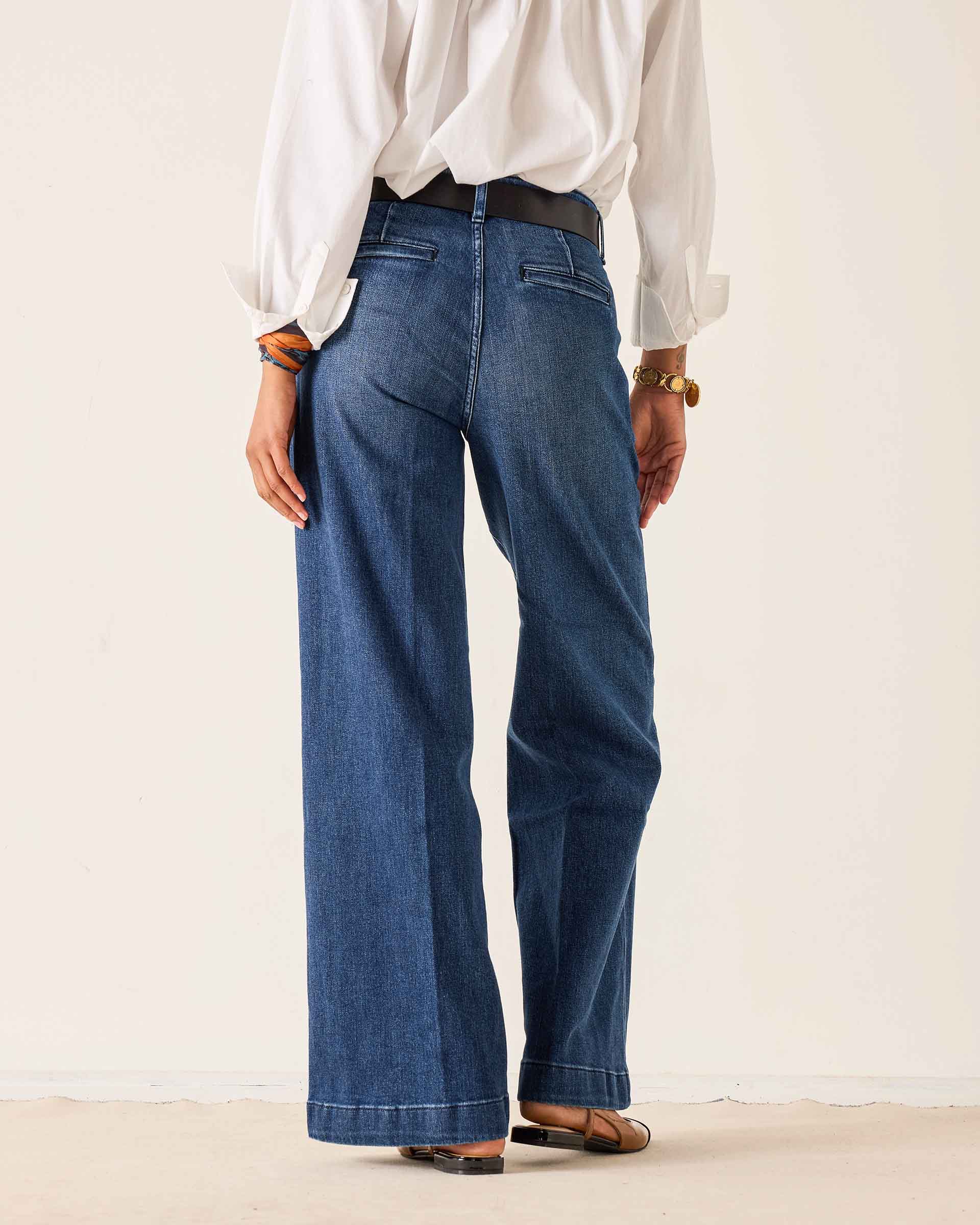 Person wearing blue jeans and a white shirt on a plain background