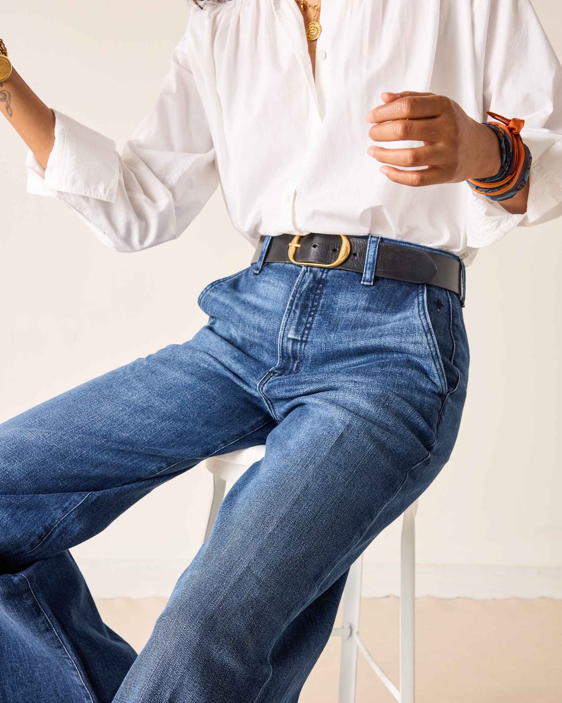 Person wearing blue jeans and a white shirt sitting on a white stool against a plain background