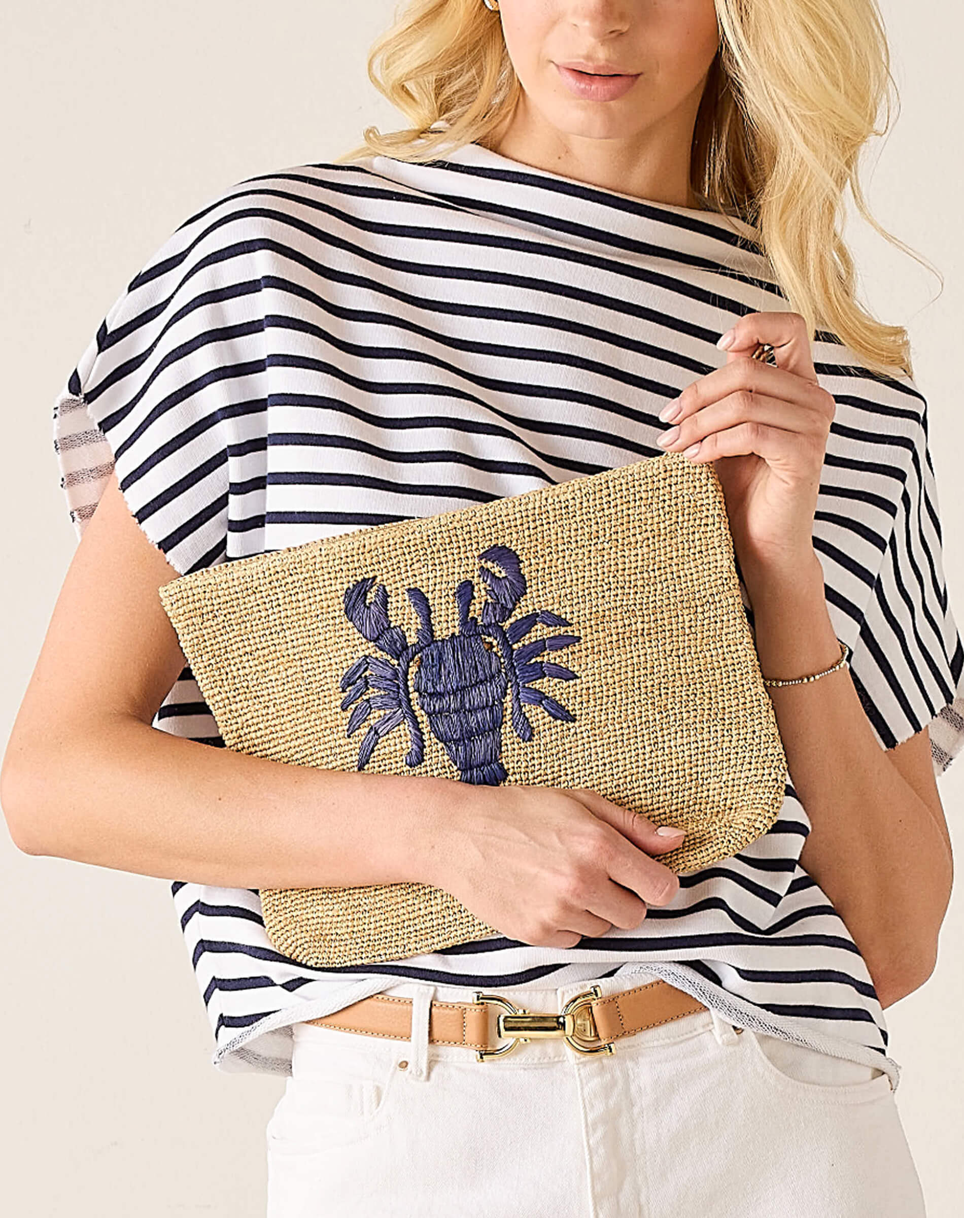 Woman holding a straw clutch with a lobster design against a neutral background