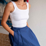 Woman wearing a white tank top and blue pants against a neutral background