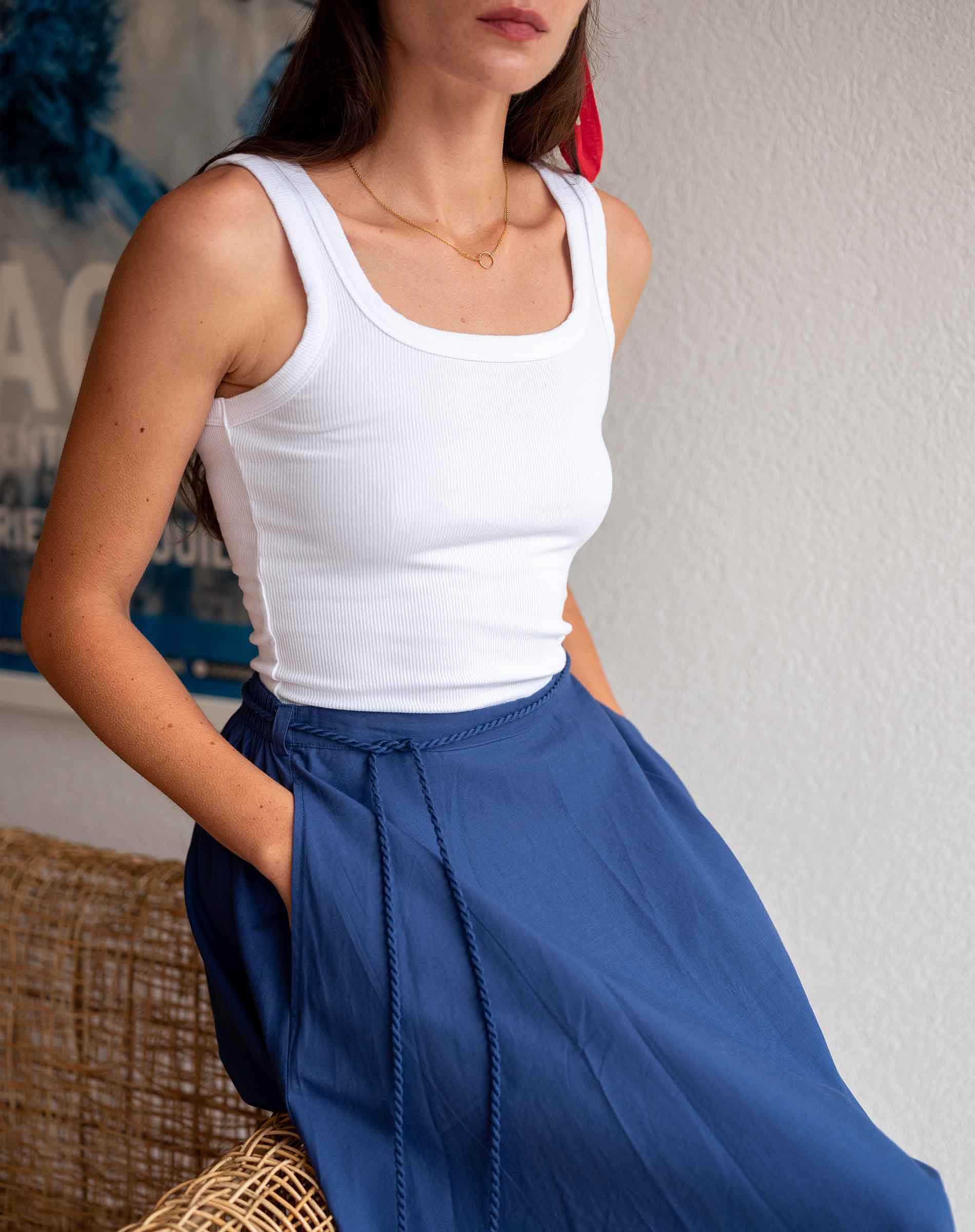 Woman wearing a white tank top and blue pants against a neutral background
