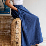 Person wearing blue wide-leg pants and a white top, sitting on a woven chair.