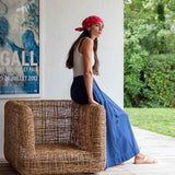 Woman sitting on a wicker chair outdoors with a poster on the wall.
