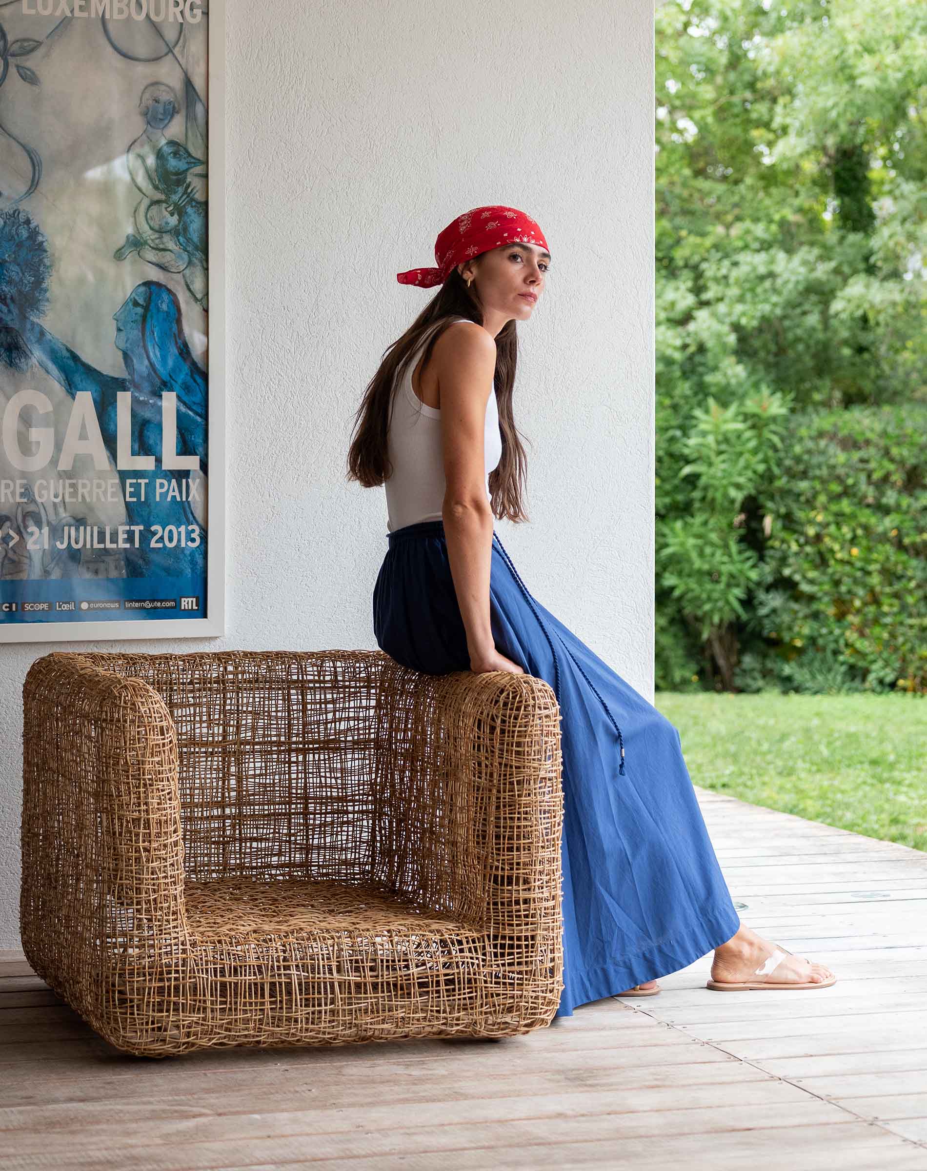 Woman sitting on a wicker chair outdoors with a poster on the wall.