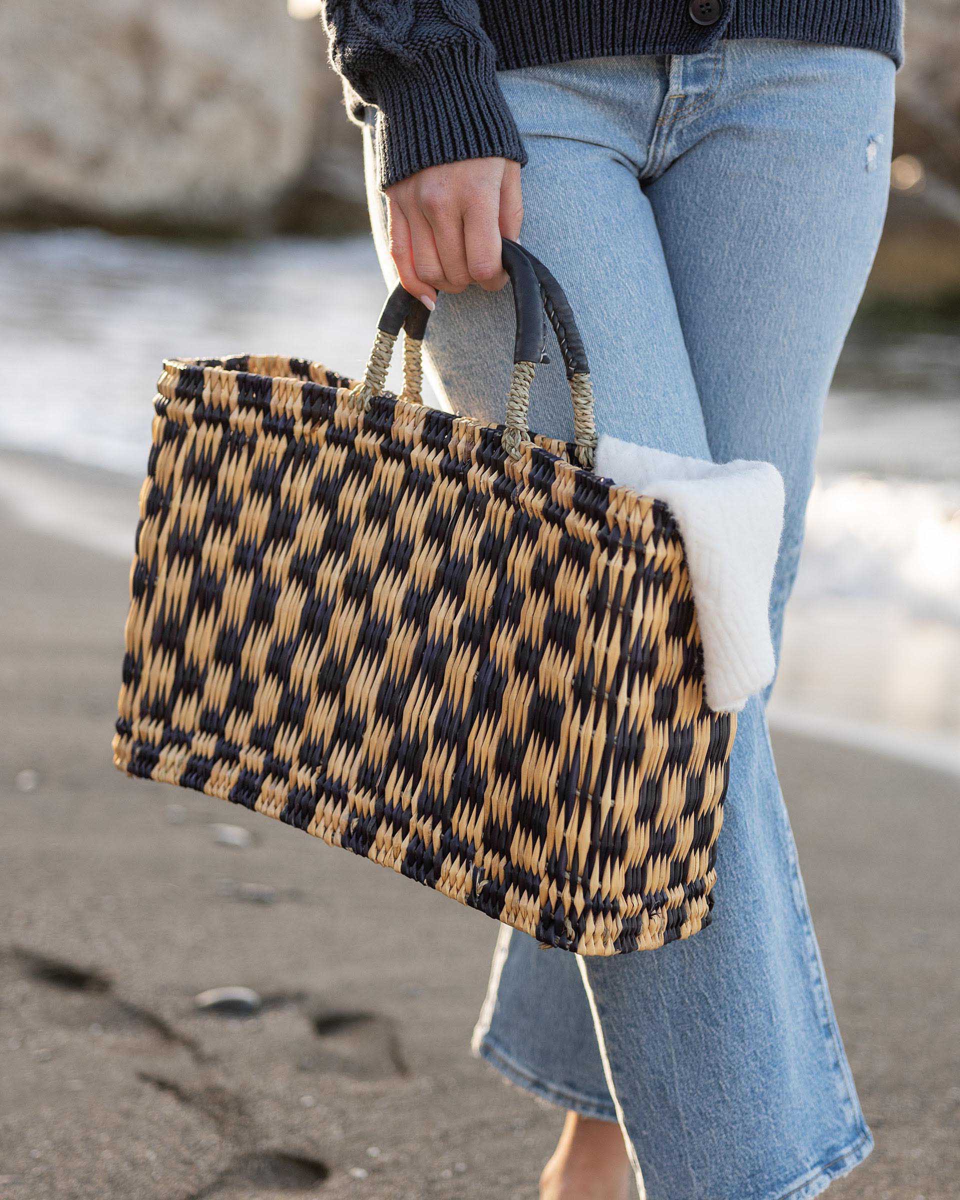 female holding medium sized straw bag with navy leather handles and a navy checkered print on beach