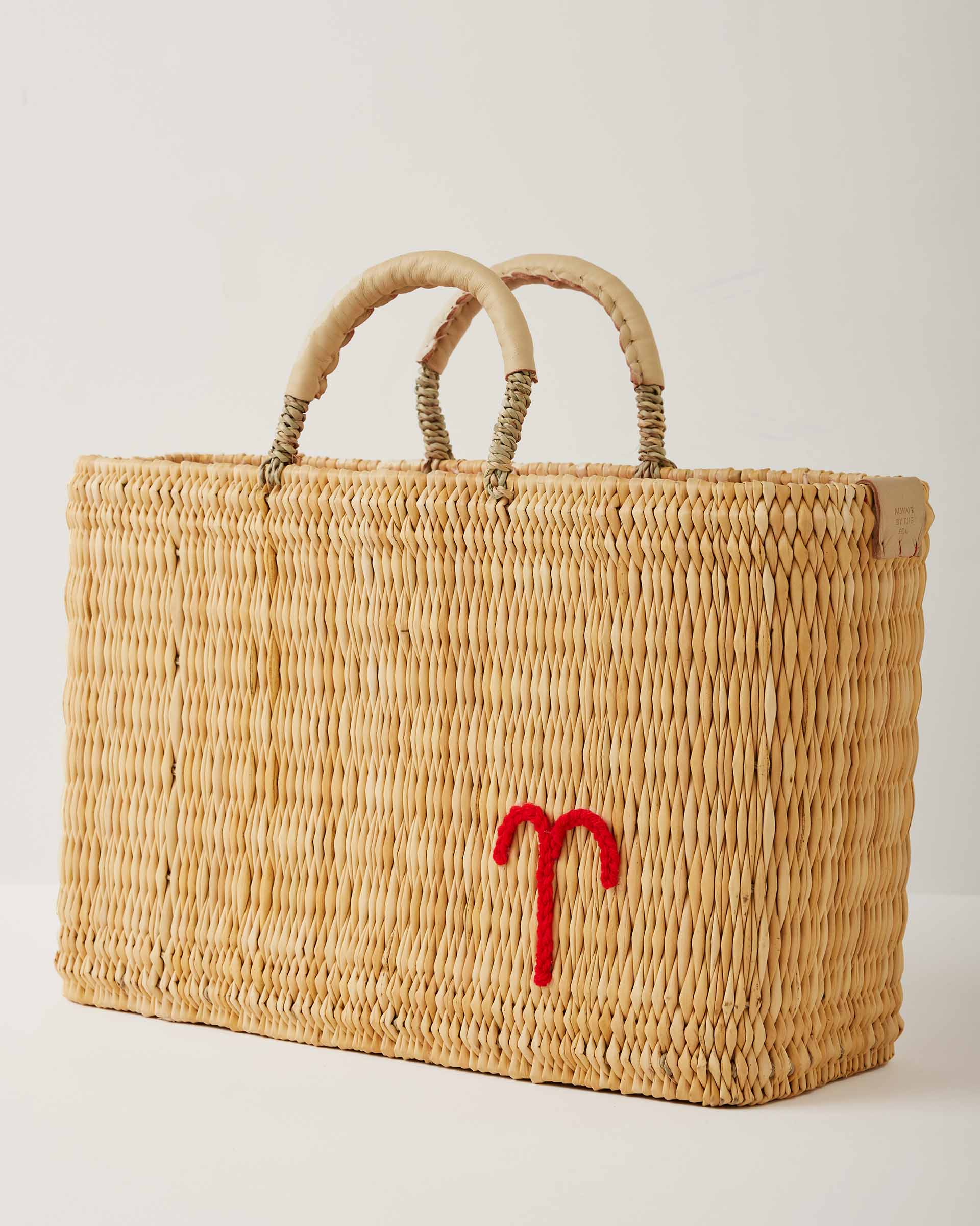 Market straw basket with tan leather handles and Aries symbol embroidered in red