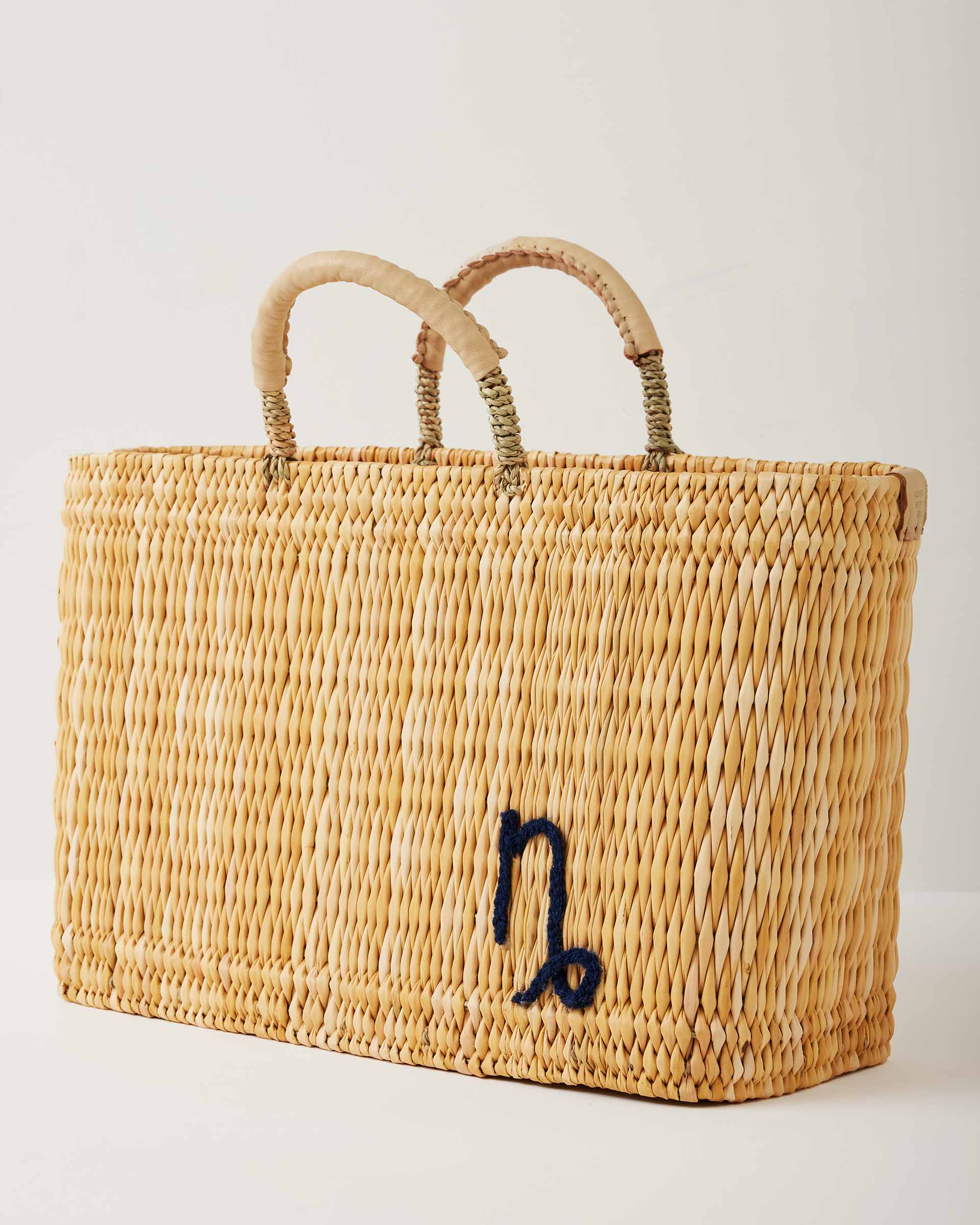 Market straw basket with tan leather handles and Capricorn symbol embroidered in black