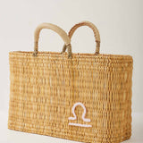 Market straw basket with tan leather handles and Libra symbol embroidered in white