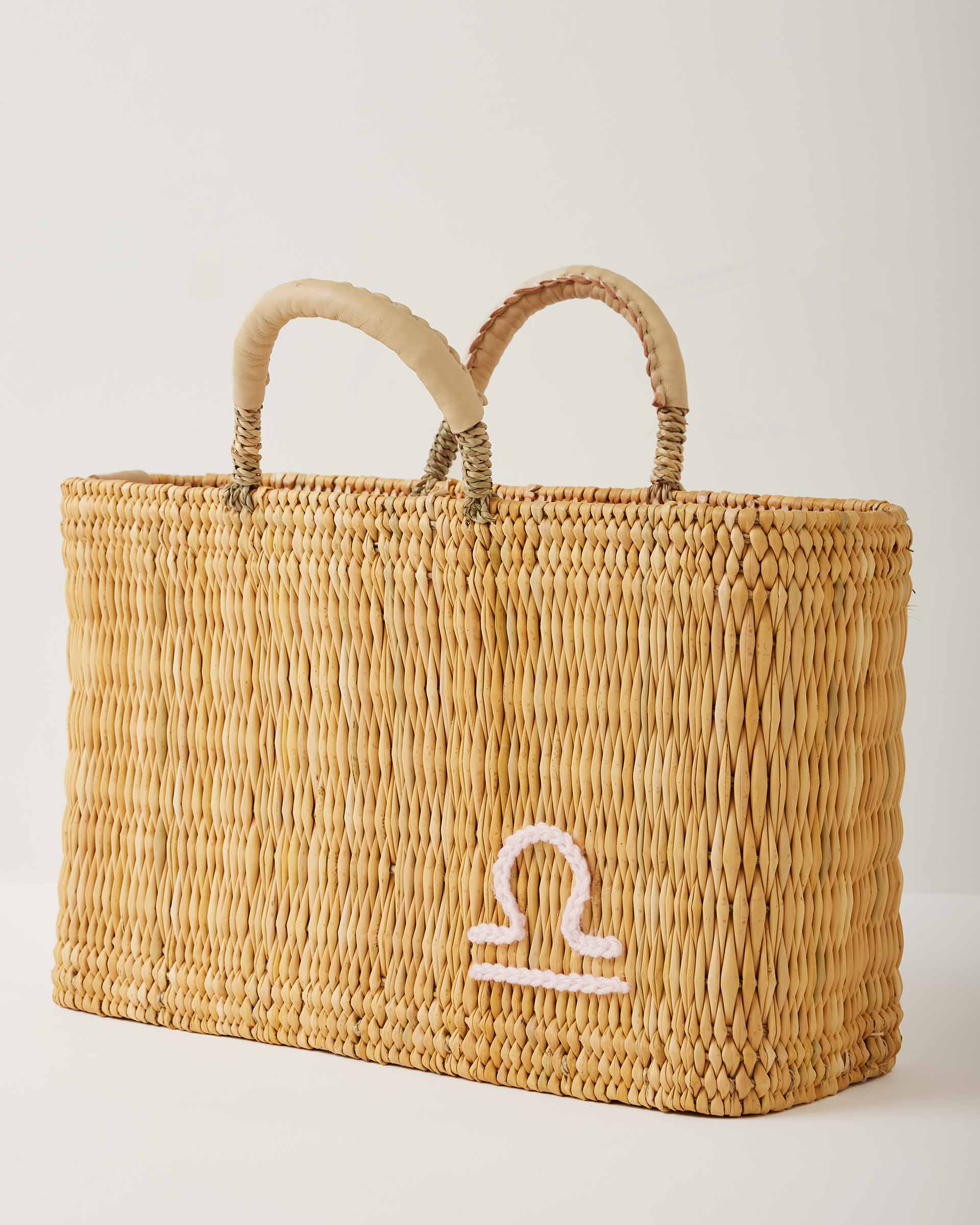 Market straw basket with tan leather handles and Libra symbol embroidered in white