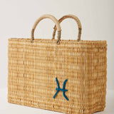 Market straw basket with tan leather handles and Pisces symbol embroidered in teal