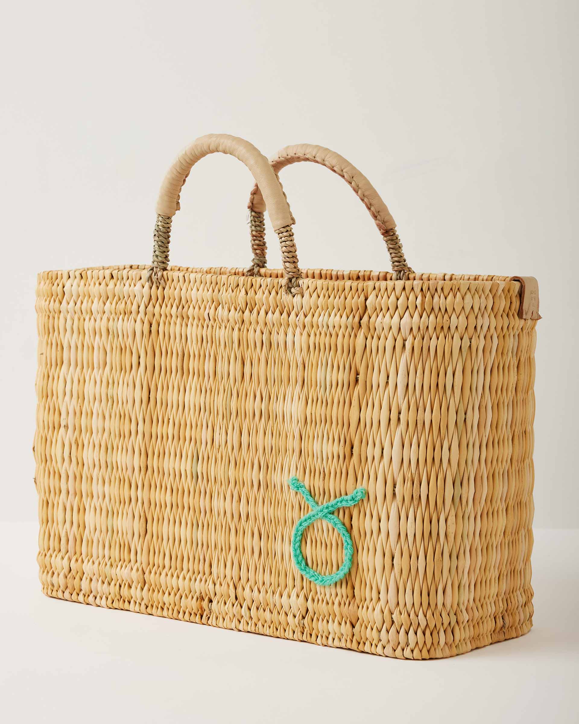 Market straw basket with tan leather handles and Taurus symbol embroidered in foam green