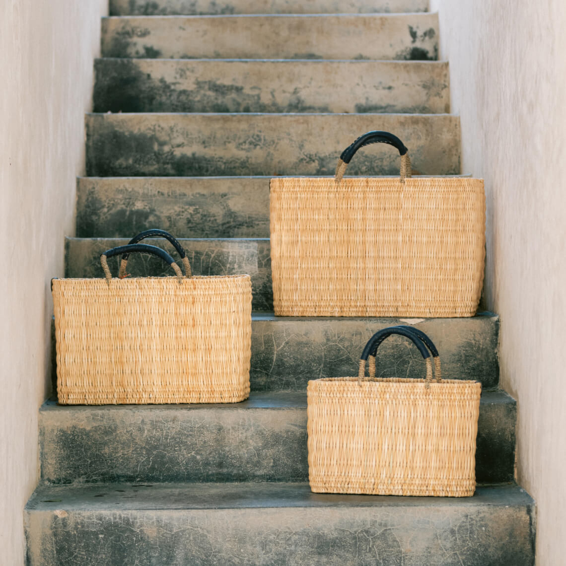 Threee different size straw woven market bag on grey stairs