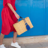 woman holding medina tassel basket wearing red dress in front of a blue door