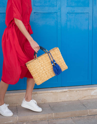 woman holding medina tassel basket wearing red dress in front of a blue door
