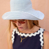 Person wearing a blue and white striped sun hat and sunglasses on a beige background
