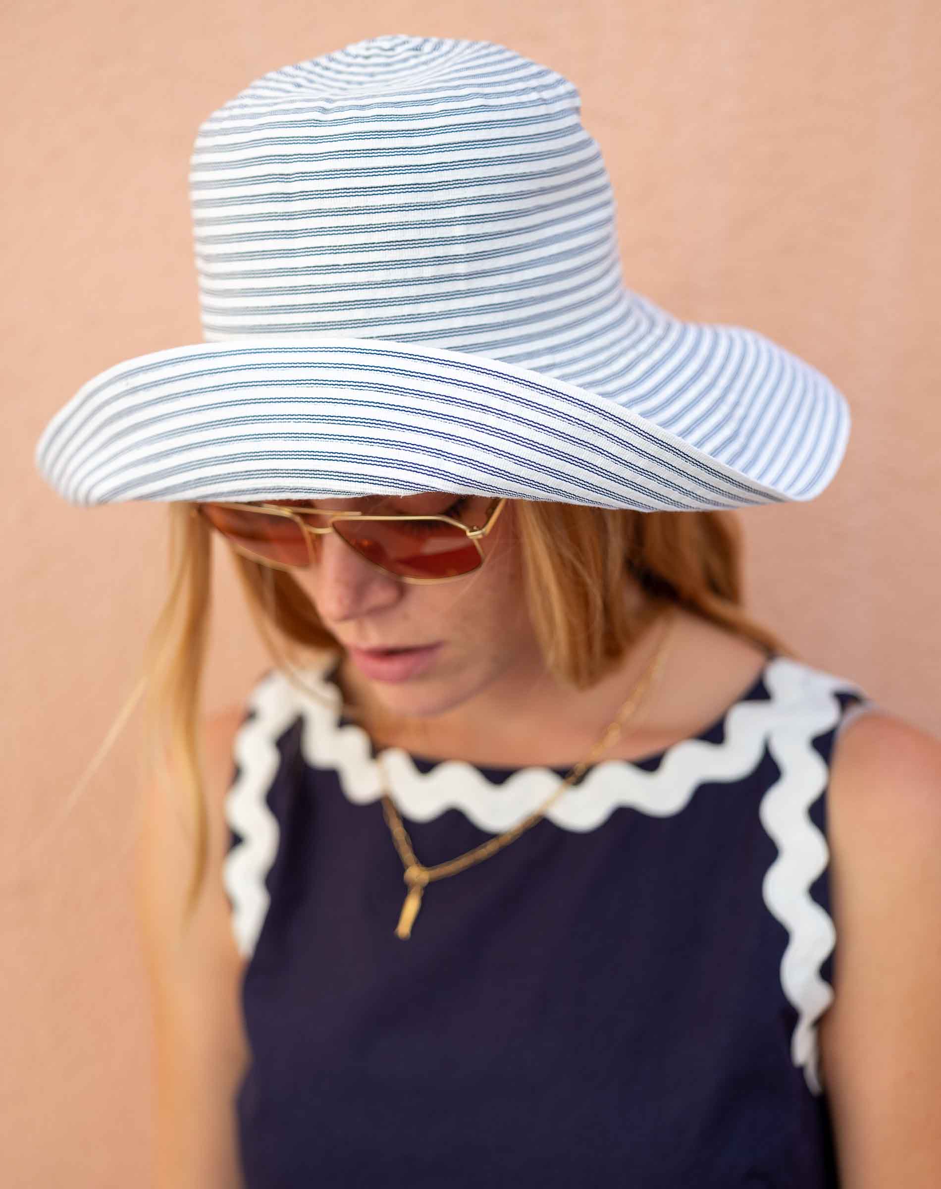 Person wearing a blue and white striped sun hat and sunglasses on a beige background