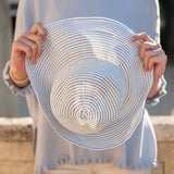 Person holding a white sun hat with blue stripes