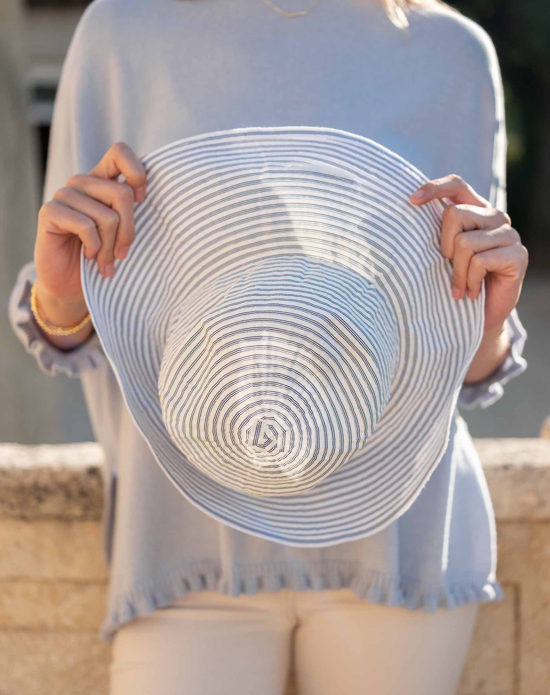 Person holding a white sun hat with blue stripes