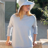 Woman wearing a light blue sweater and sun hat outdoors