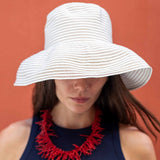 Woman wearing a white sun hat and red necklace against an orange background