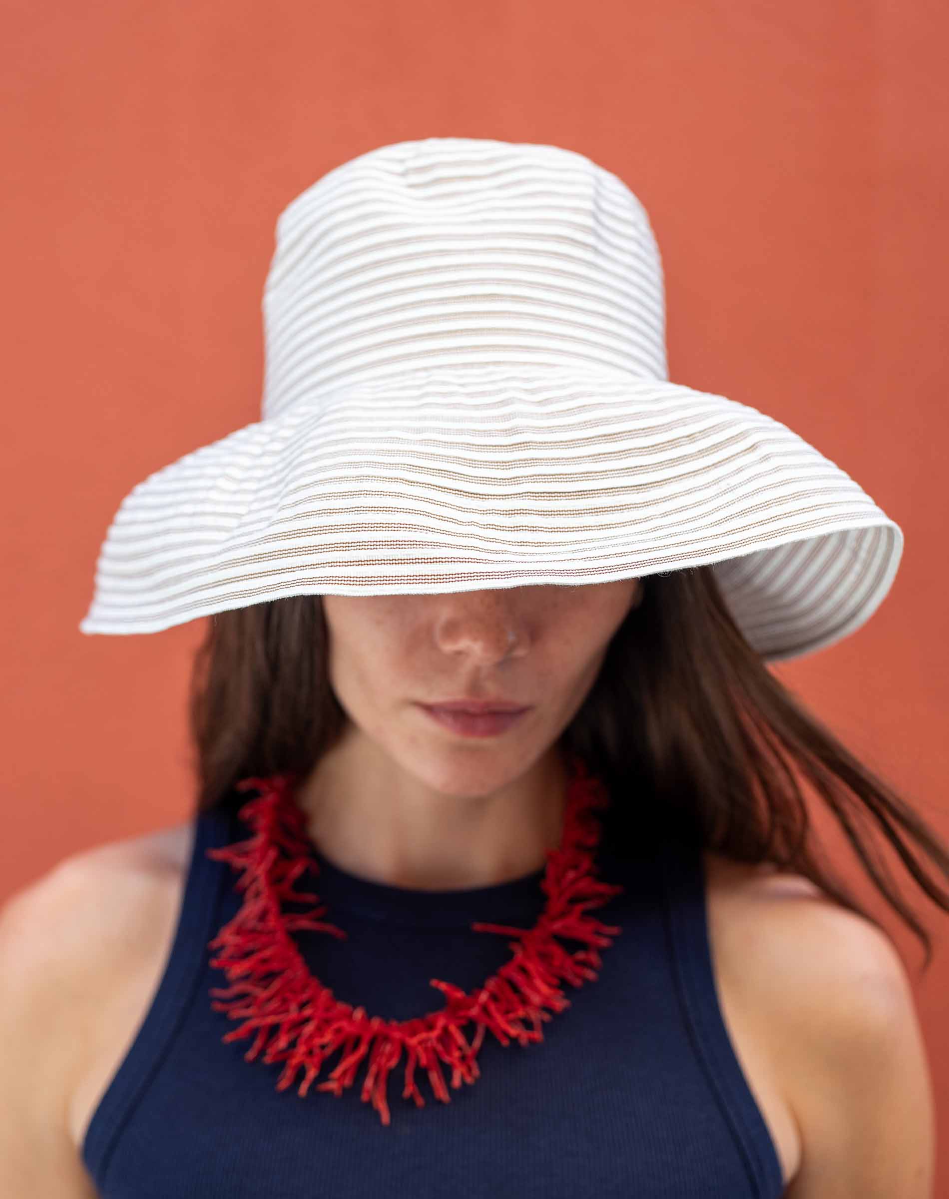 Woman wearing a white sun hat and red necklace against an orange background