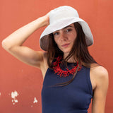 Woman wearing a white sun hat and blue dress with a red necklace against a red wall.
