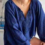 Woman wearing a blue blouse with lace detailing sitting indoors.