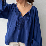 Woman wearing a blue blouse with lace details and white shorts against a plain background