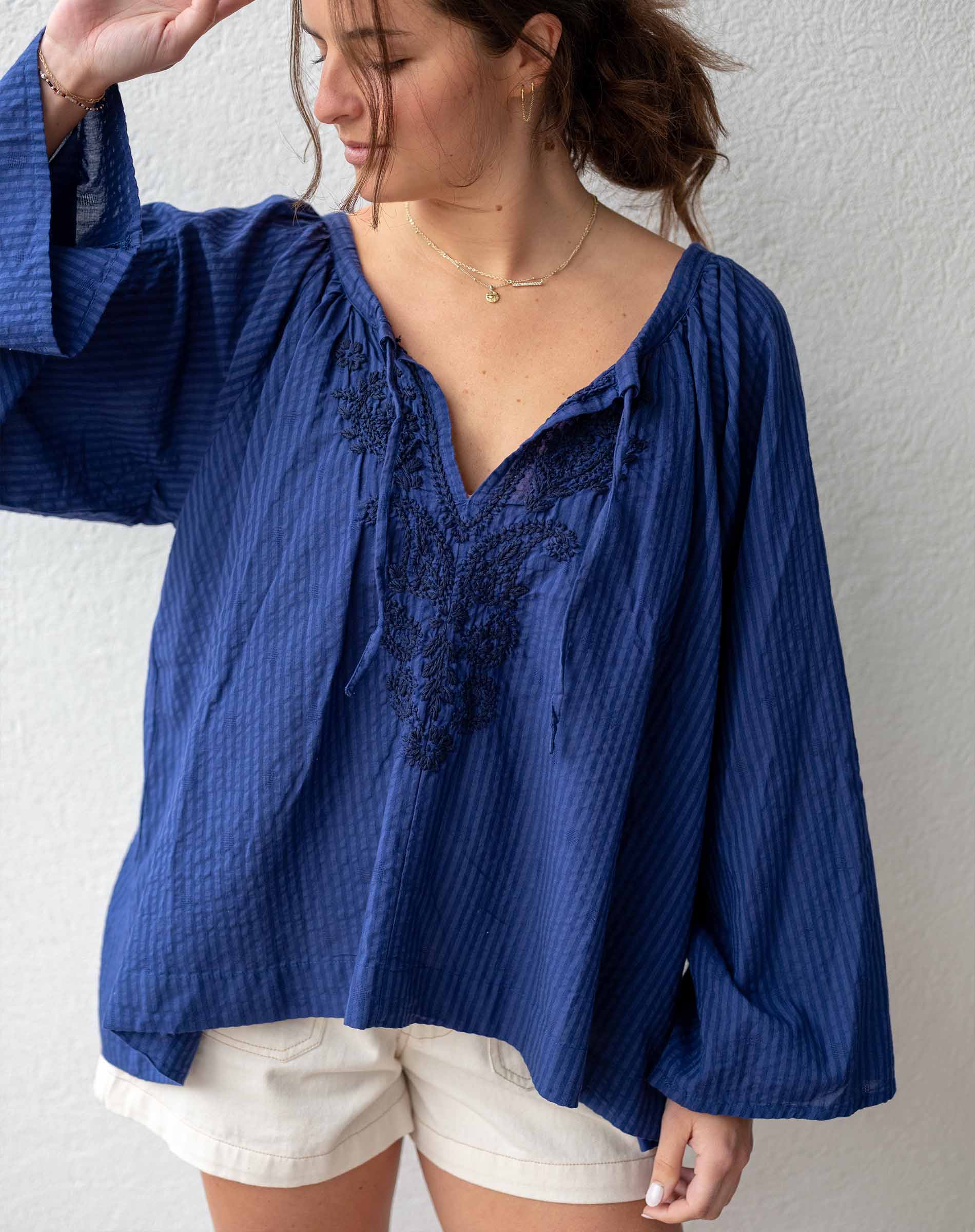 Woman wearing a blue blouse with lace details and white shorts against a plain background