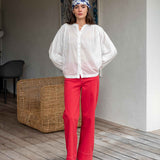 Woman wearing a white blouse and red pants standing in a room with a textured wall and wicker basket.