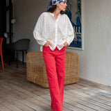 Woman wearing a white blouse and red pants with a blue patterned headscarf indoors.