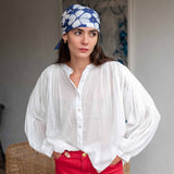 Woman wearing a white blouse, red pants, and a blue headscarf with white patterns.