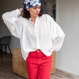 Woman wearing a white blouse and red pants with a blue headscarf featuring white floral patterns.