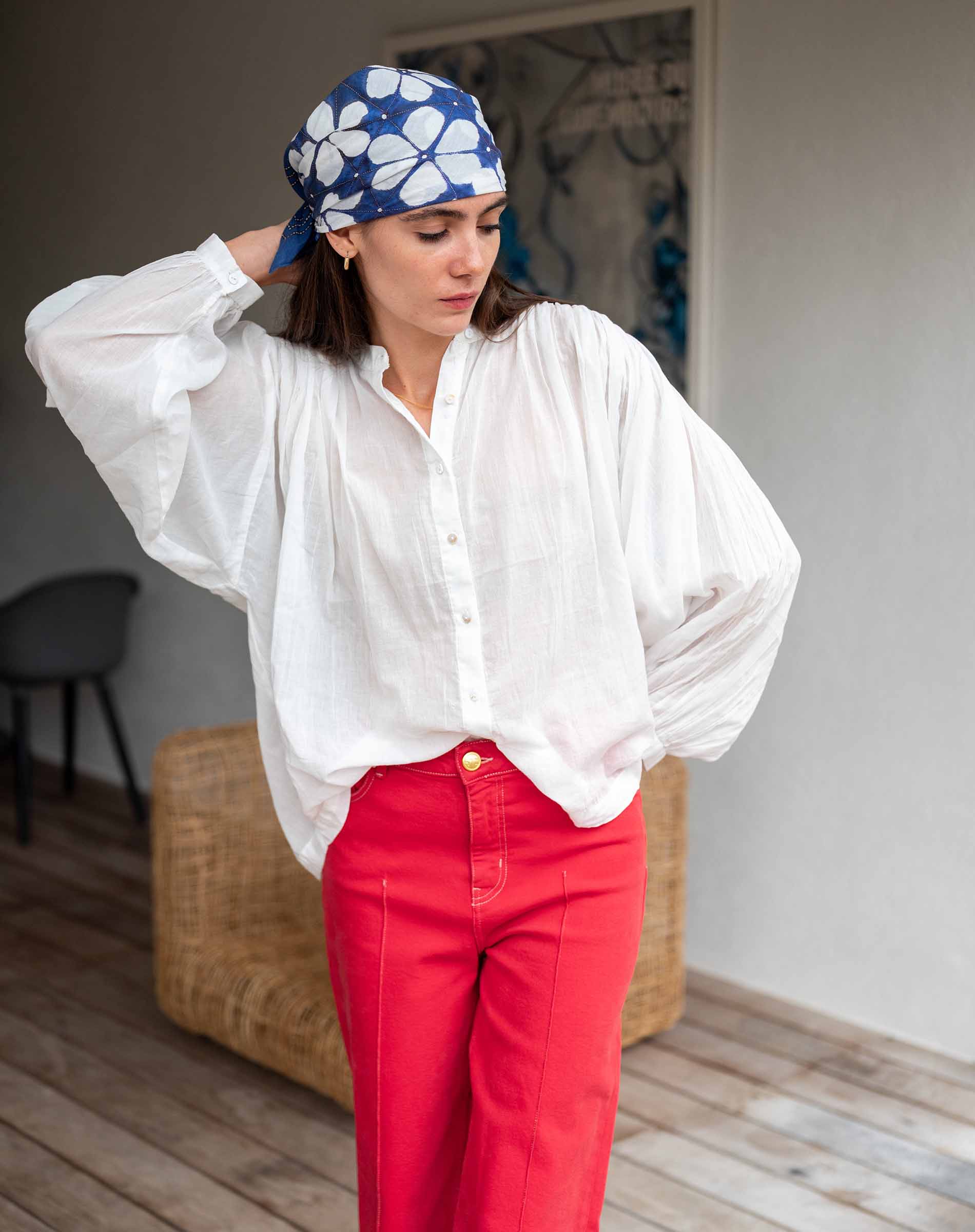 Woman wearing a white blouse and red pants with a blue headscarf featuring white floral patterns.